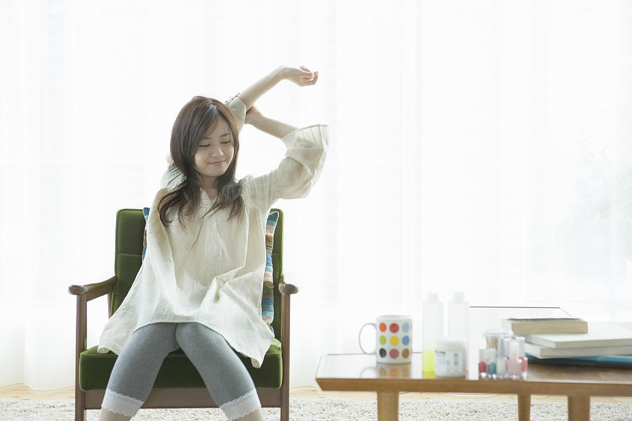 Young woman stretching arms on armchair Photograph by Indeed
