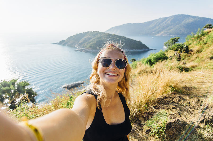 Young woman takes selfie, on hillside above sea Photograph by Andrii Lutsyk/ Ascent Xmedia