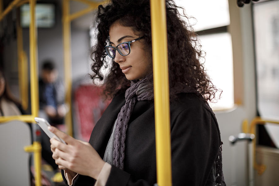 Young woman traveling by bus and using smart phone Photograph by Damircudic