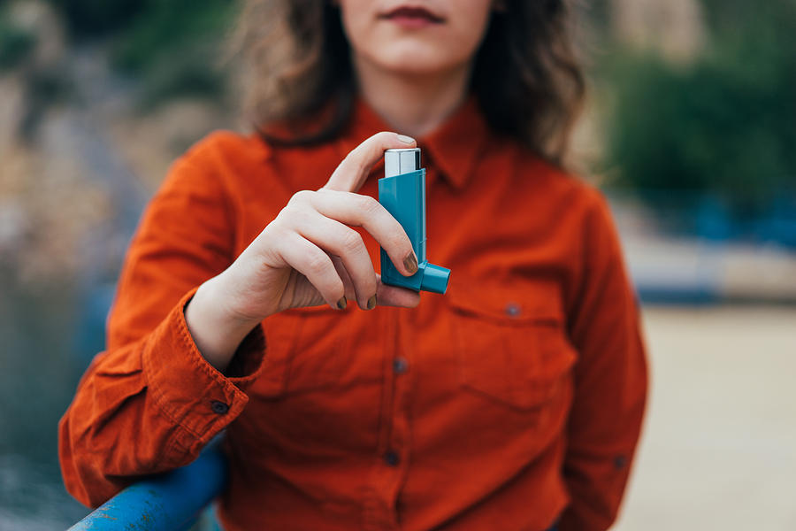Young woman using an asthma inhaler outdoors Photograph by Hsyncoban