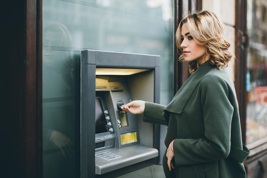 Young woman using ATM Photograph by Eclipse_images
