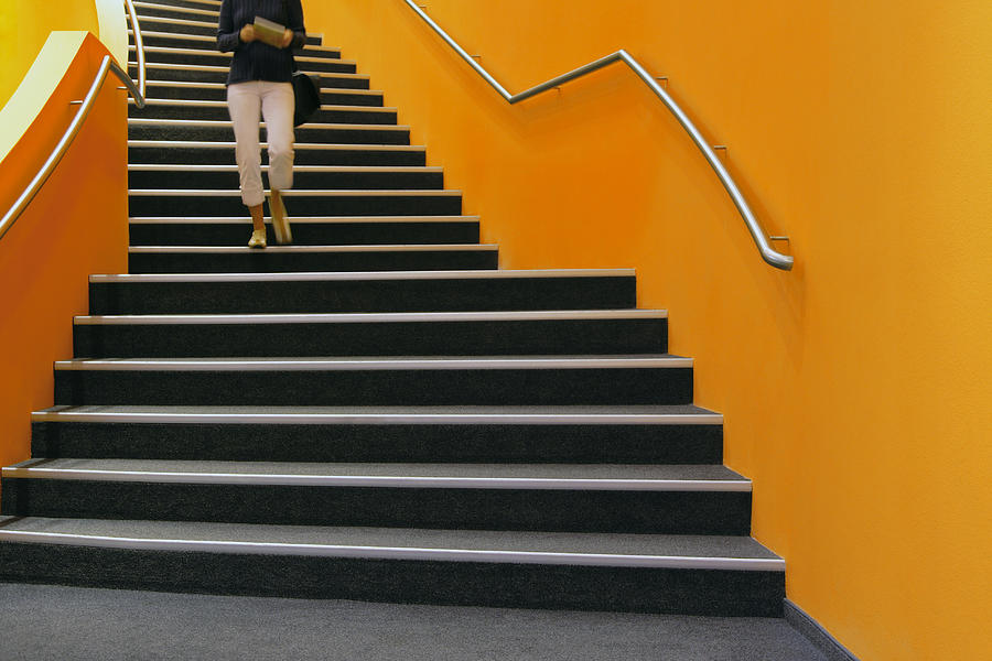 Young woman walking down orange stairs, reading book Photograph by B&M Noskowski