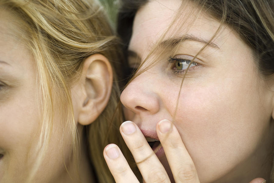 Young woman whispering secret into friends ear, close-up Photograph by ZenShui/Eric Audras