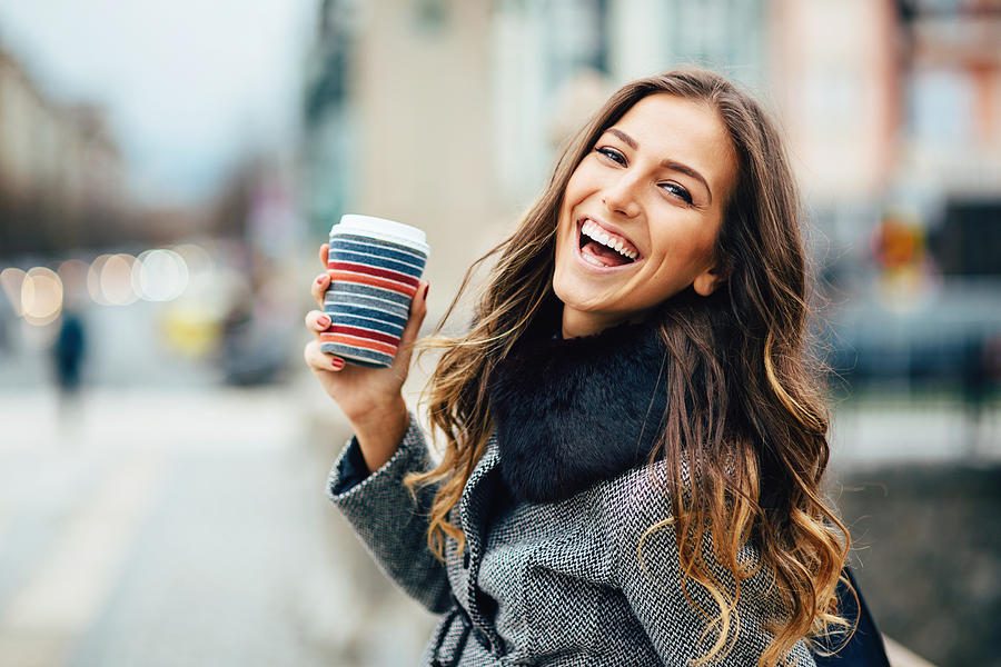Young woman with coffee cup smiling outdoors Photograph by Pixelfit