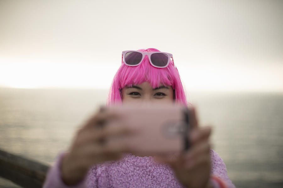 Young woman with pink hair taking a photo with her mobile phone Photograph by Eternity in an Instant
