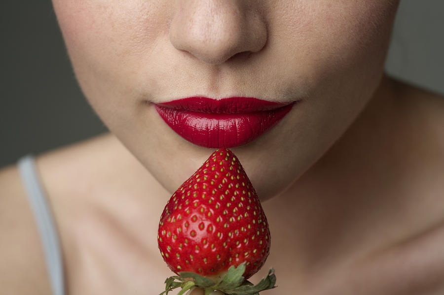 Young woman with red lips eating a strawberry (part of), close-up Photograph by Stock4b-rf