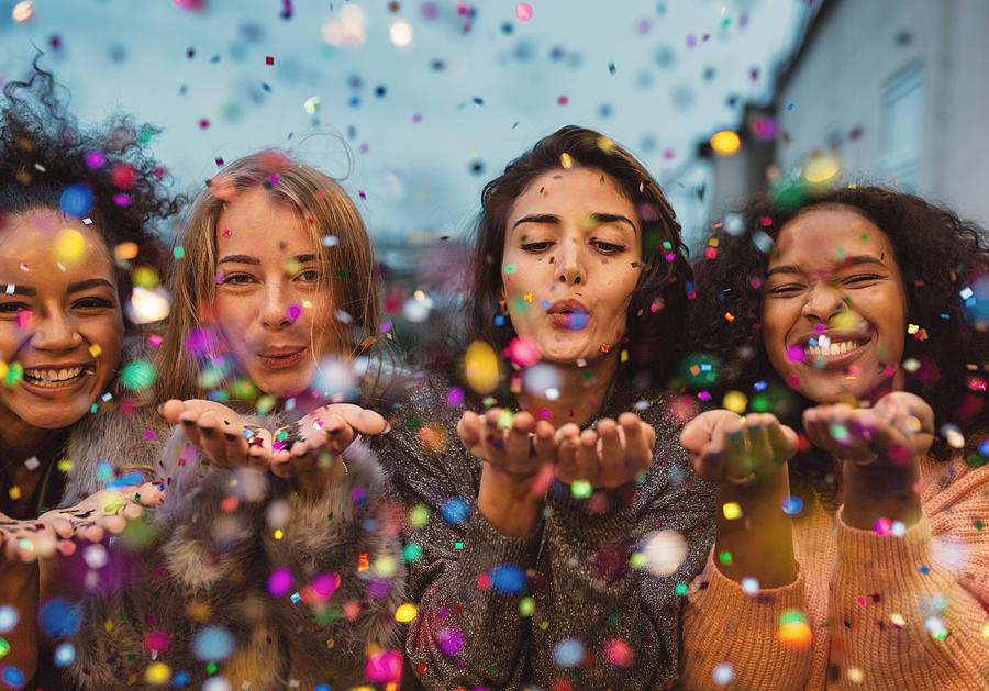 Young women blowing confetti from hands. Photograph by Youngoldman