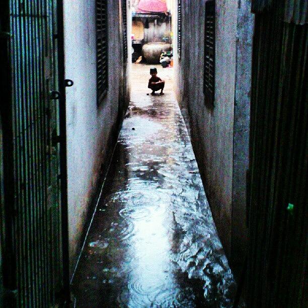 Cambodia Photograph - A boy is playing on back alley in heavy rain. by Sandman JP