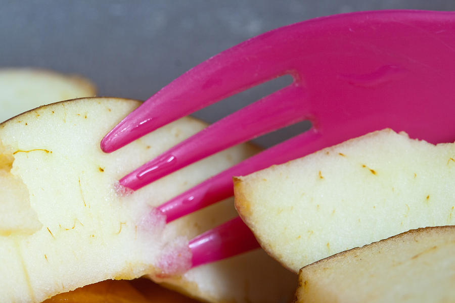 A plastic fork being used to cut into a piece of cut apple pieces Photograph by Ashish Agarwal