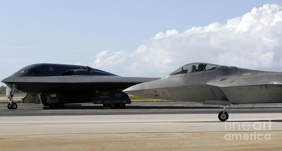 Airplane Photograph - An F-22 Raptor Taxis While A B-2 Spirit by Stocktrek Images