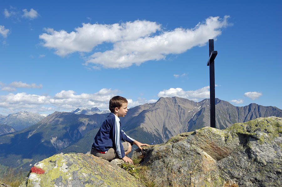 Boy on mountain top looking at cross Photograph by Matthias Hauser