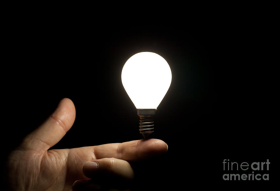 Lit light bulb balancing on finger Photograph by Simon Bratt