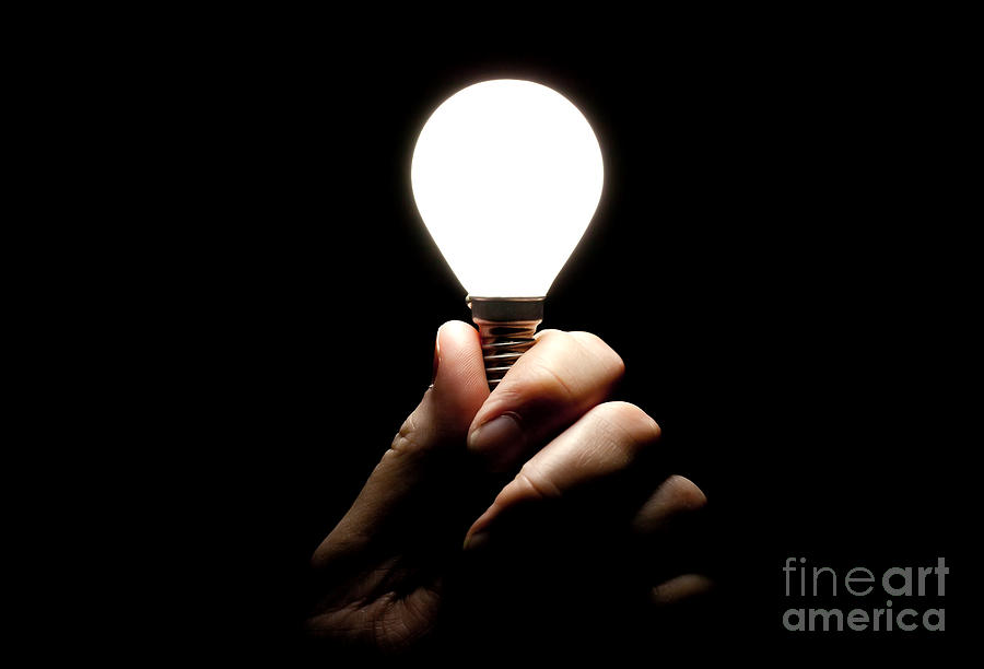 Lit lightbulb held in hand Photograph by Simon Bratt