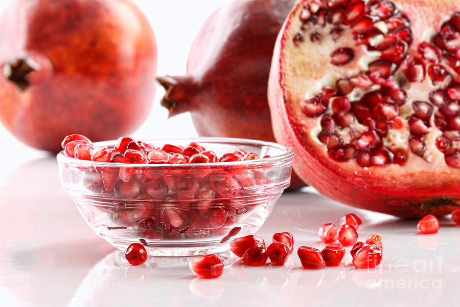 Ripe pomegranates and glass bowl of seeds on white Photograph by Sandra Cunningham
