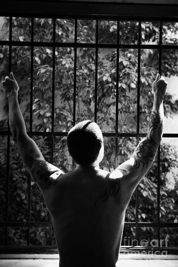 Man Photograph - Tatooed Man Stretching Arms Out On Security Safety Cage Across Open Window by Joe Fox