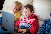 Two Boys Using A Laptop Sitting On Sofa Photograph by Science Photo Library