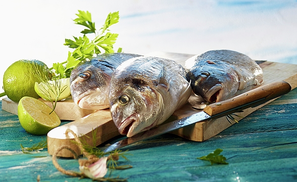 Three Gilt-head Bream On A Wooden Board With Limes And Herbs