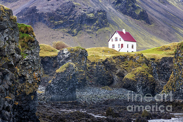 Jane Rix - Arnarstapi, Iceland. A view of the craggy coastline with a solitary house. Autumn colours with mountains in the background. Snaefellsnes peninsula.