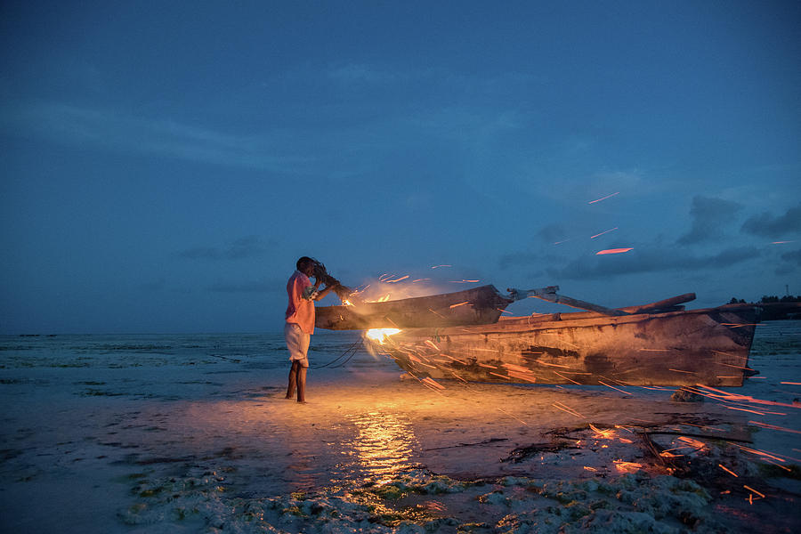 A local fisherman uses flame to repair his boat at sunset by Gareth Pickering A local fisherman uses flame to repair his boat at sunset by Gareth Pickering