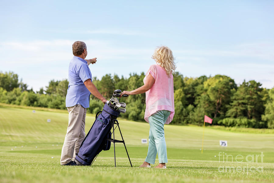 Active senior couple playing golf on a course. #1 Photograph by Michal Bednarek
