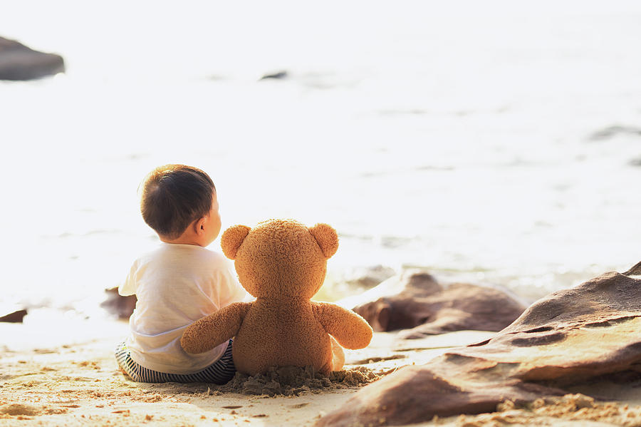 Baby and teddy bear sit togather on the beach #1 Photograph by Anek Suwannaphoom