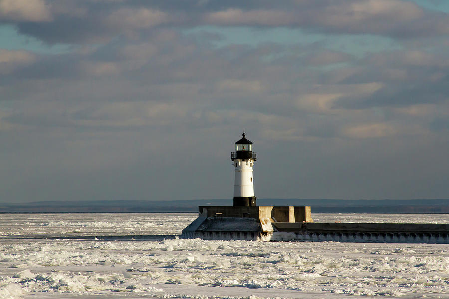 Frozen Lake Superior shoreline with lighthouse and shipping pier ...