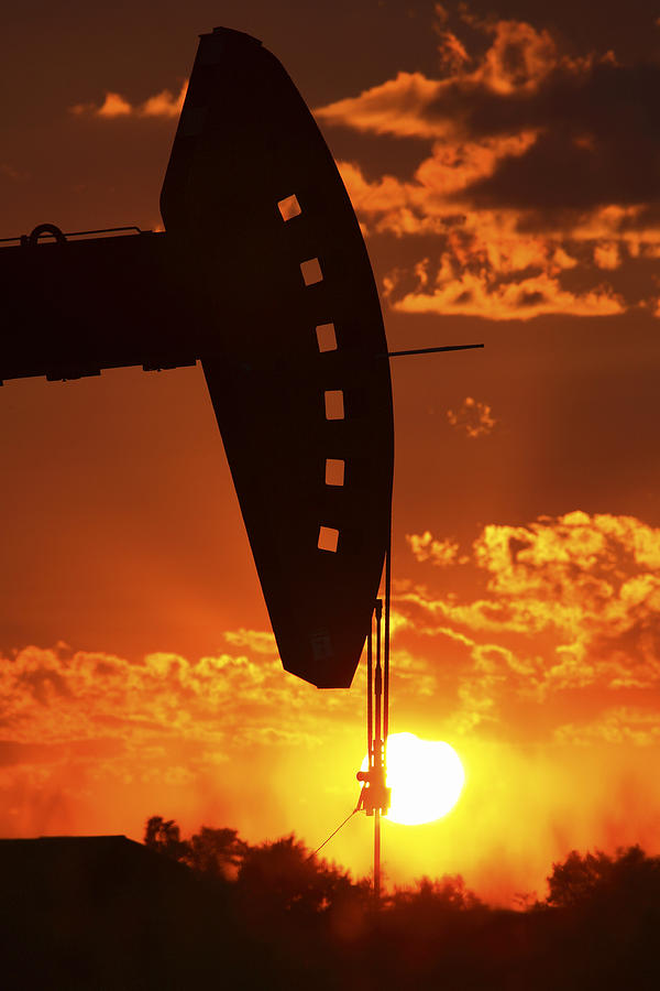 Oil rig pump jack silhouetted by setting sun #1 Photograph by Mark Duffy