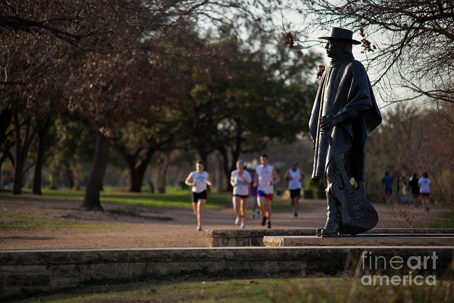 Sports Photograph - Runners and joggers pass by the Stevie Ray Vaughan Memorial Statue on Lady Bird Town Lake hike and bike trail #1 by Dan Herron