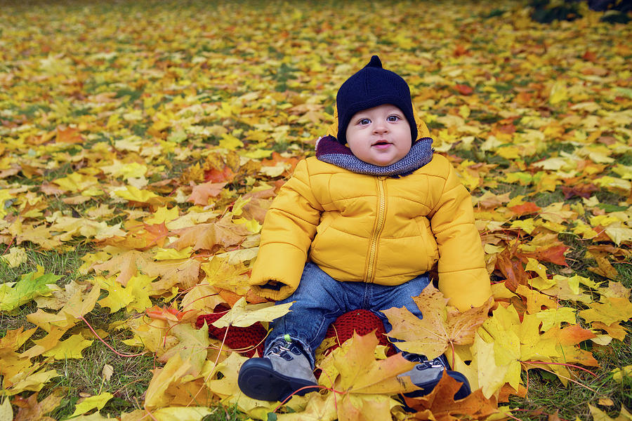 Child In A Yellow Jacket And Scarf And Hat Sitting On The Ground Photograph