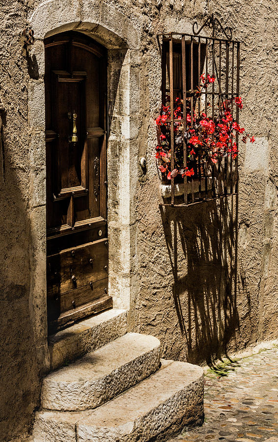 A barred window and door with Red Begonia and contrasty shadows Saint Paul De Vence France Photograph by Maggie Mccall