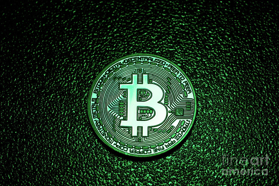 A coin with bitcoin logo in a green lighting. Photograph by Michal Bednarek