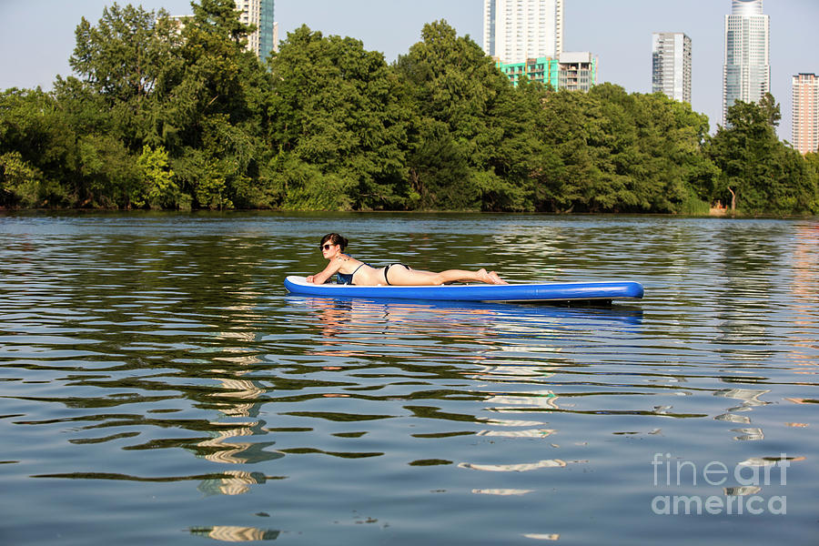 Woman Photograph - A female stand up paddle board lounges on the crystal clear blue waters of on Lady Bird Lake in Austin, Texas- Stock Image by Dan Herron