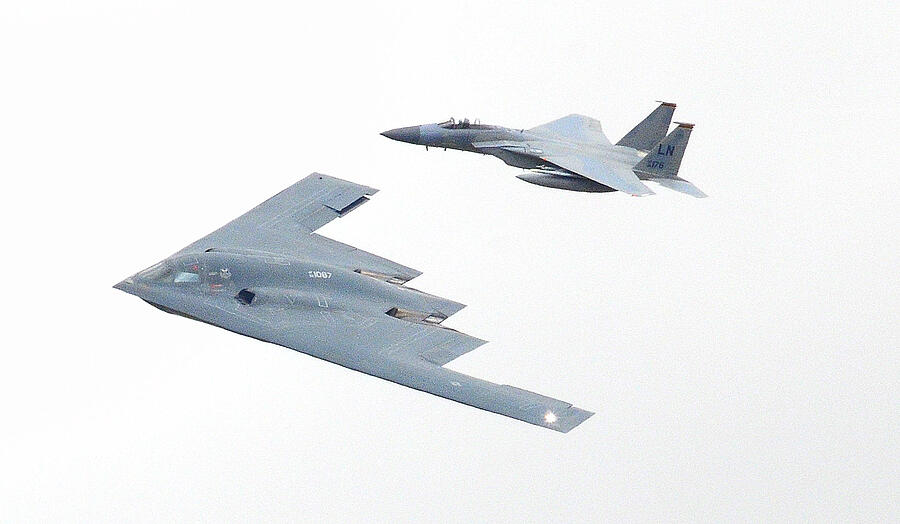 A Northrop Grumman B-2 Spirit stealth bomber escorted by a F-15 Eagle Fighter Jet Photograph by Gordon James
