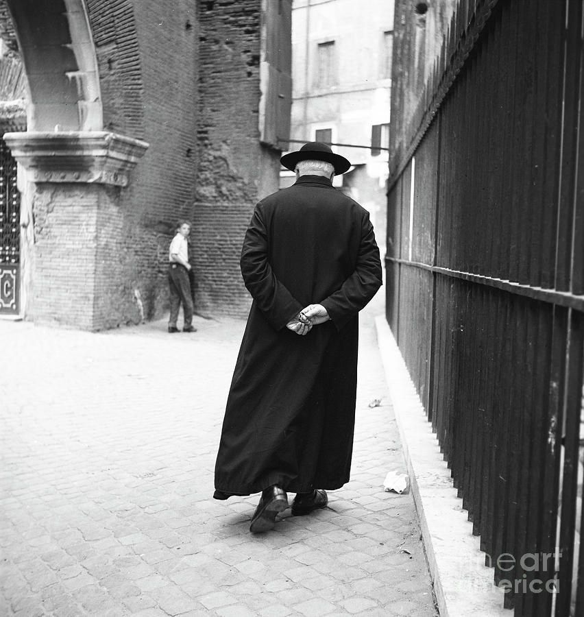 Rome Photograph - A priest walks down a street in Rome, 1955 by The Harrington Collection Rome Photograph - A priest walks down a street in Rome, 1955 by The Harrington Collection