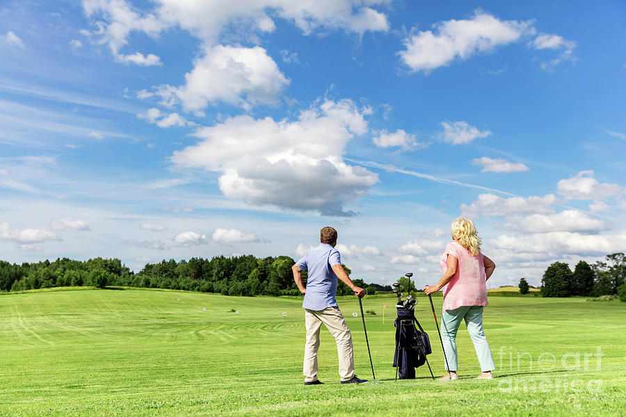Active senior couple playing golf on a course. Photograph by Michal Bednarek