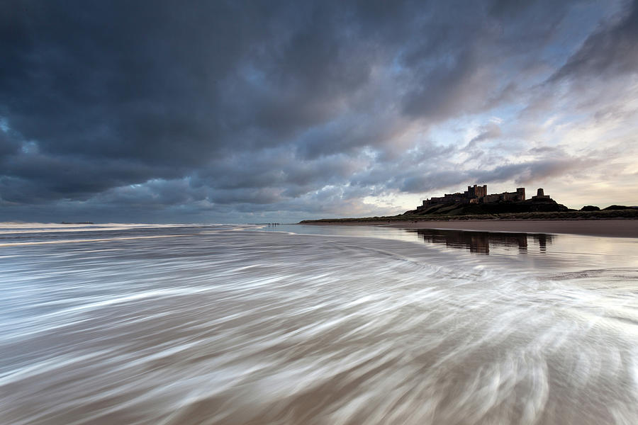 Bamburgh Castle at high tide in the surf Photograph by Anita Nicholson