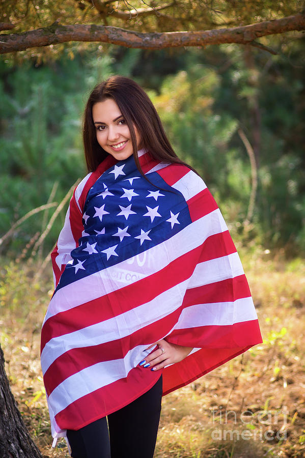 Beautiful model poses with the flag of the USA in the summer park ...