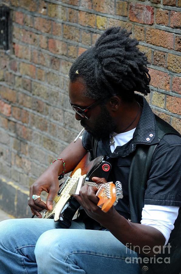 Black street musician sits against wall plays guitar London England Photograph by Imran Ahmed