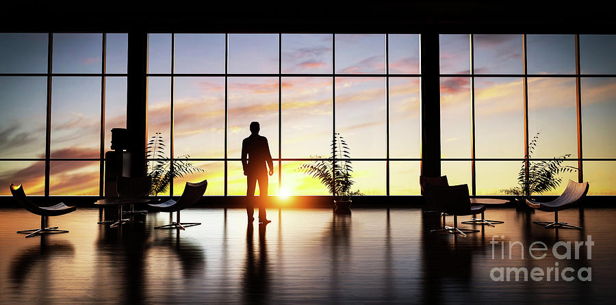 Business man standing in the office looking out of the window at sunset sky. Photograph by Michal Bednarek