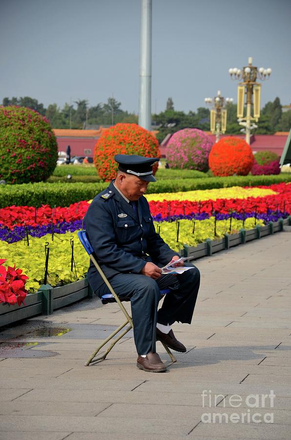 Chinese security guard reads in front of flower display Beijing China Photograph by Imran Ahmed