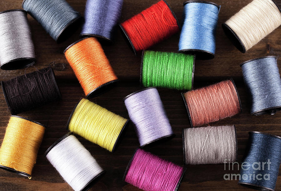 Colorful cotton reels scattered on dark wood Photograph by Simon Bratt