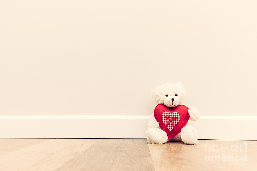 Cute teddy bear with big red plush heart. Sitting on wooden floor against white wall Photograph by Michal Bednarek