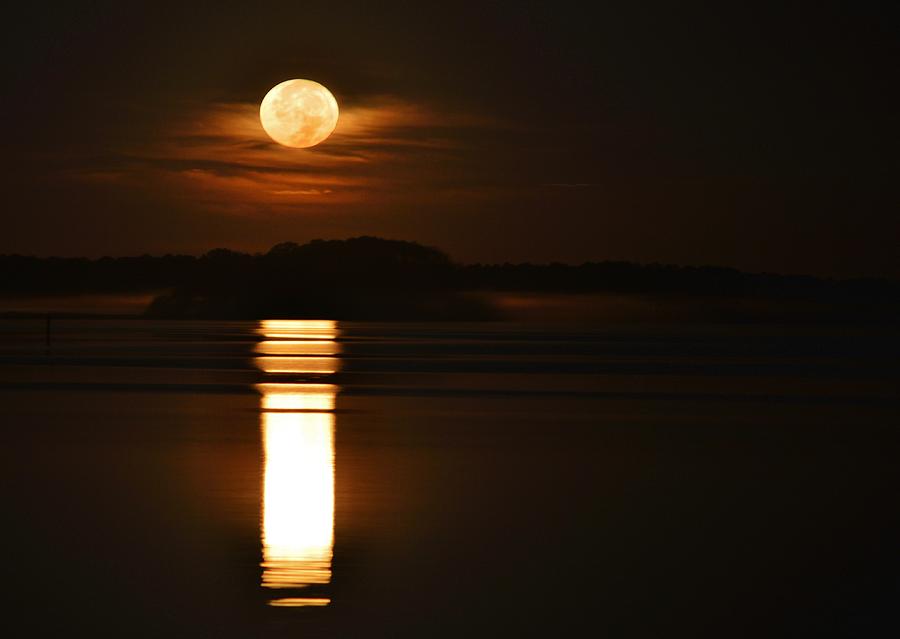 Morning Moon - A large moon reflects off of a calm bay as it hangs in the clouds above the horizon Photograph by Billy Beck