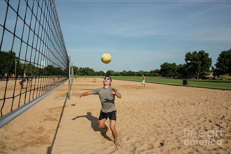 Sports Photograph - Fit man playing volleyball sets up the ball under a clear blue sky on the sand volleyball courts at Zilker Park by Dan Herron