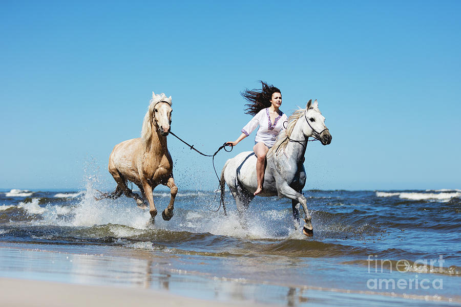 Girl galopading through the sea with two horses. Photograph by Michal Bednarek
