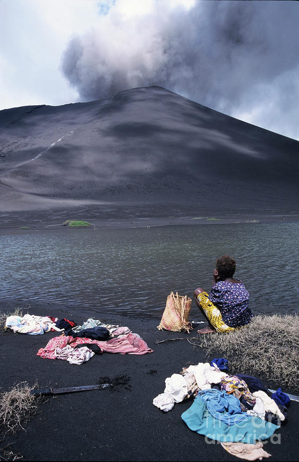 Girl washing clothes in a lake with the Mount Yasur volcano emitting smoke in the background Photograph by Sami Sarkis