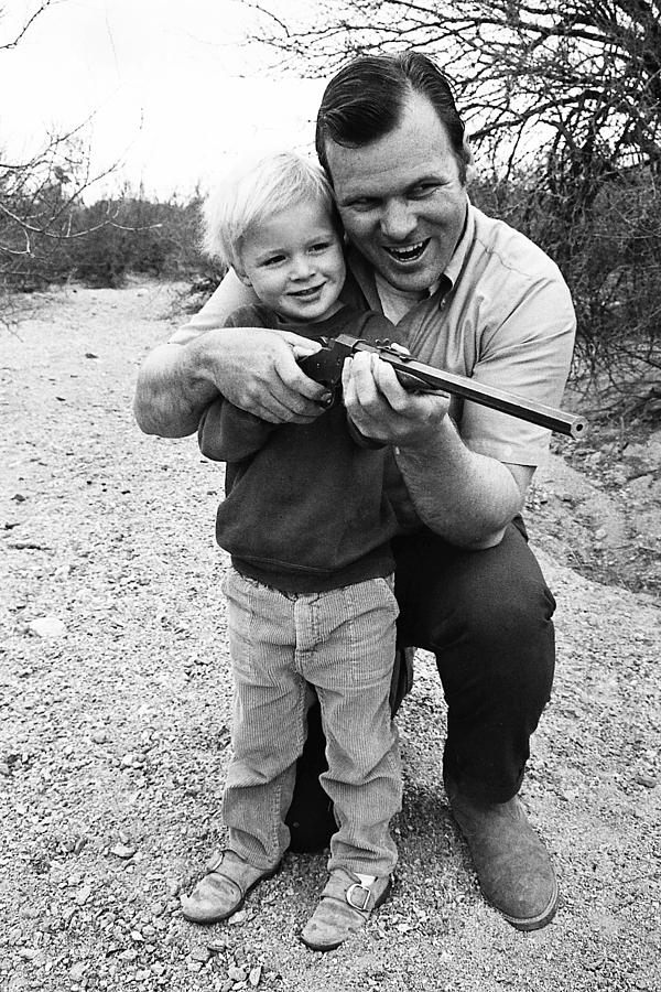 Grinning Barry Sadler with son Baron aiming toy rifle Tucson Arizona 1971 Photograph by David Lee Guss