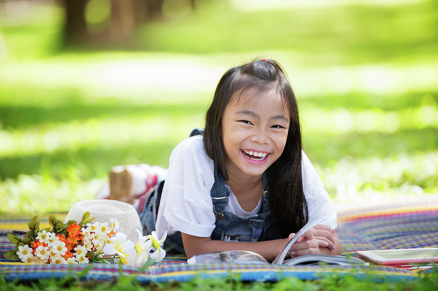 Happy asian girl sitting on grass and read a magazine book Photograph by Anek Suwannaphoom