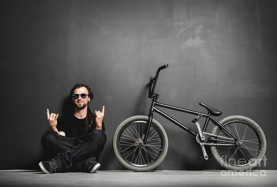 Happy man sitting next to his BMX bike, showing rocker gesture. Photograph by Michal Bednarek