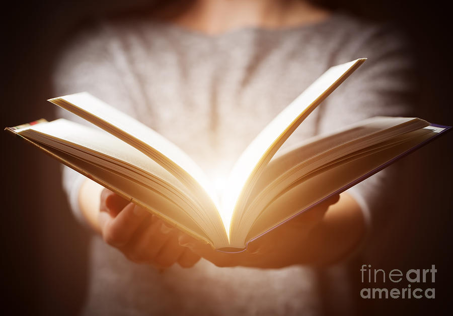 Light coming from book in womans hands in gesture of giving Photograph by Michal Bednarek